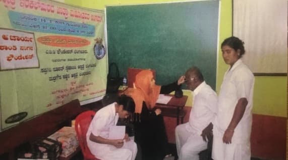 A doctor consulting patients at a table beneath Kannada camp banners.