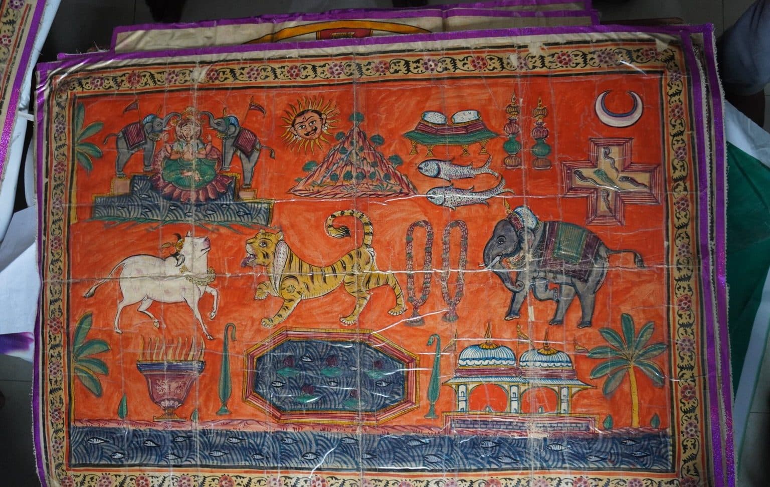 An orange painted leaf showing an elephant, a white bull, a lion, a crescent moon, fish and vessels.