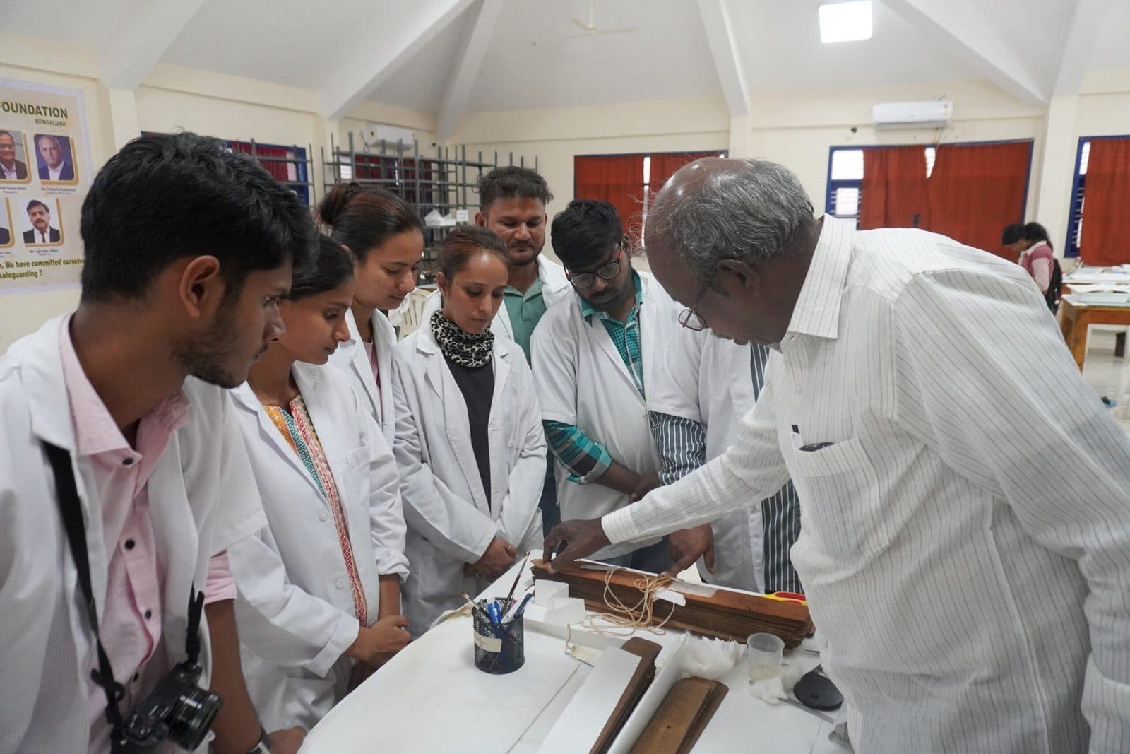 Conservators in white coats and visitors gathered around a table of palm leaves.
